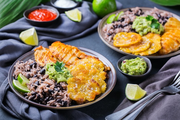 Comida tradicional centroamericana caribeña cubana colombiana. Arroz con frijoles negros, pechuga de pollo frita rostizada y tostones, plátanos verdes fritos con salsa de guacamole