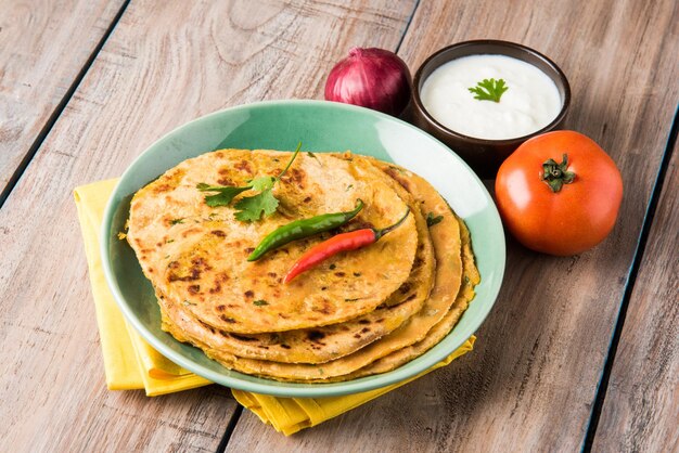 Comida tradicional india Aloo paratha o pan plano relleno de patata. servido con salsa de tomate y cuajada sobre fondo de colores o madera. Enfoque selectivo