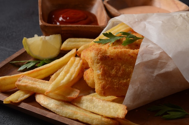 Comida tradicional inglesa - Fish and Chips. Filés de peixe frito e batata frita crocante servidos com ketchup e molho de tarter caseiro.