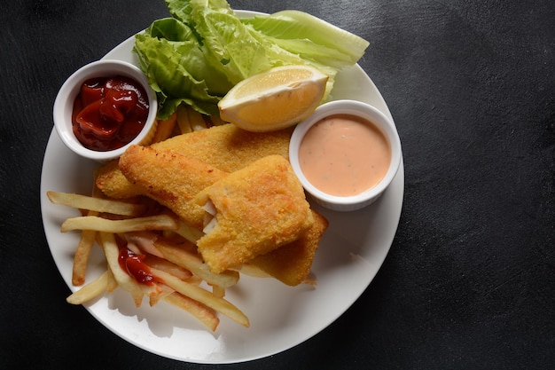 Comida tradicional inglesa - Fish and Chips. Filés de peixe frito e batata frita crocante servidos com ketchup e molho de tarter caseiro.
