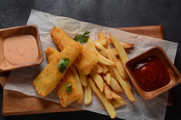 Comida tradicional inglesa: pescado y patatas fritas. Filetes de pescado frito y crujientes patatas fritas servidos con salsa de tomate y salsa tártara casera.