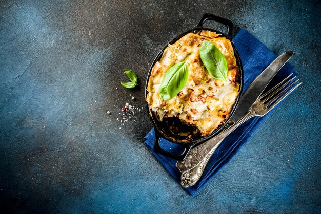 Comida tradicional italiana, lasaña casera con albahaca fresca, fondo azul oscuro