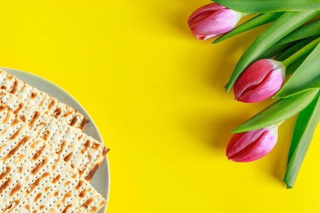 Foto comida tradicional judía pan matzo y tulipanes rosados sobre un fondo amarillo feliz pascua fiesta religiosa de primavera pascua copia el espacio