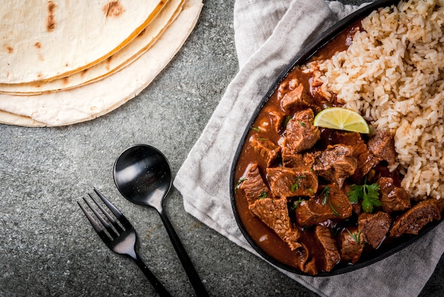 Comida tradicional mexicana e americana Guisado de carne com tomate e especiarias pimenta - Chile Colorado Com tortilhas de arroz cozido com limão