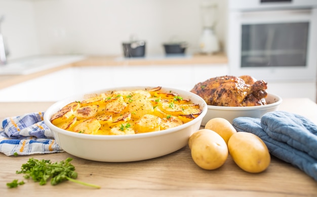 Comida tradicional patatas asadas y pollo entero en la mesa de la cocina de casa.