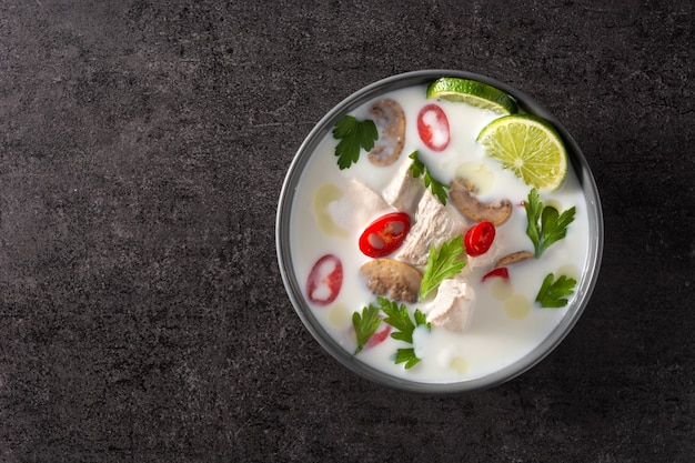 Comida tradicional tailandesa tom kha gai sopa de leite de coco com frango, gengibre, pimenta, limão e cogumelos no preto