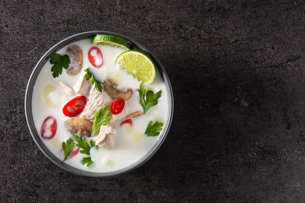 Comida tradicional tailandesa Tom Kha Gai sopa de leche de coco con pollo, jengibre, guindillas, lima y champiñones sobre negro