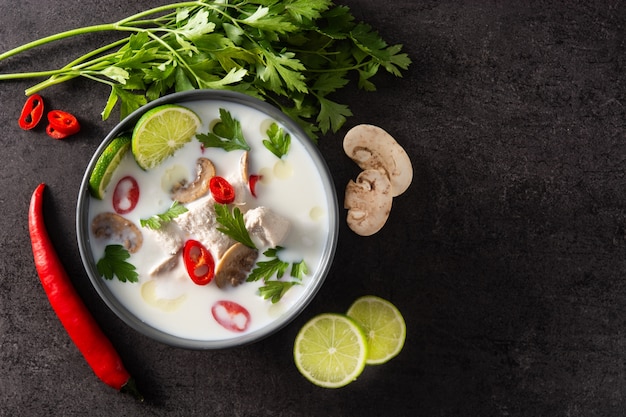 Comida tradicional tailandesa Tom Kha Gai sopa de leche de coco con pollo, jengibre, guindillas, lima y champiñones sobre negro