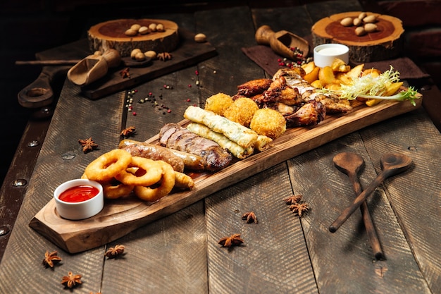 Comida variada frita na tábua de madeira com molhos