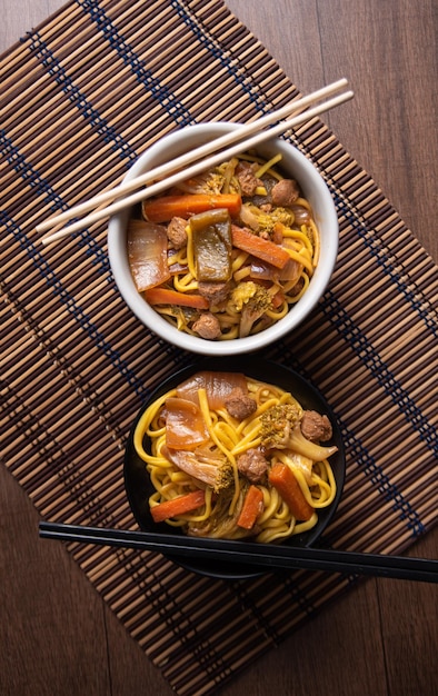 Comida vegan Yakisoba vegano com pauzinhos em uma tigela na esteira de bambu sobre a vista superior de madeira