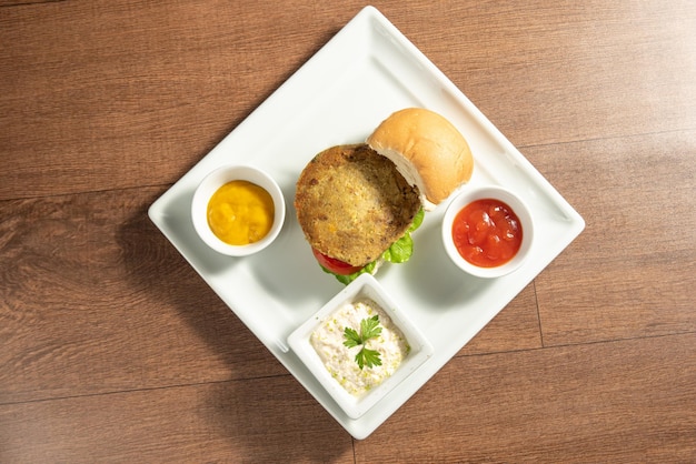 Comida vegana Hamburguesa vegana y salsas en un plato blanco sobre la vista superior de madera