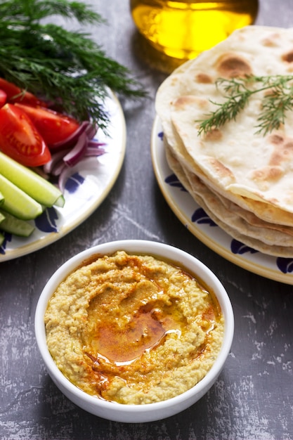 Comida vegana, hummus casero con pan plano, verduras y aceite de oliva sobre un fondo de hormigón.