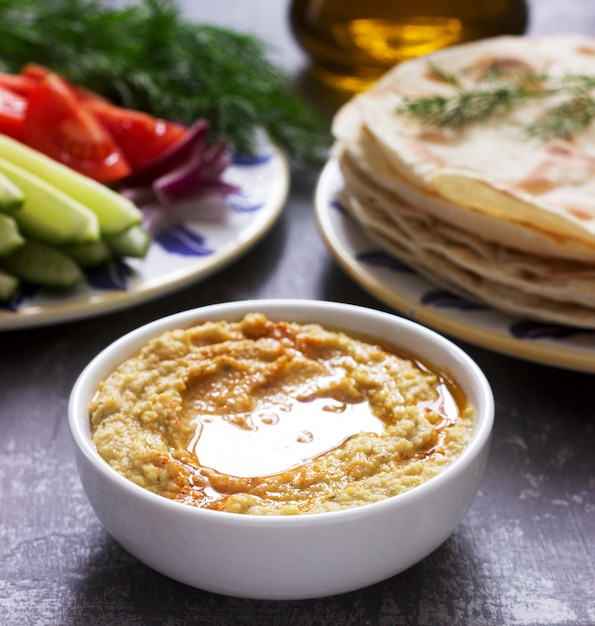 Comida vegana, hummus casero con pan plano, verduras y aceite de oliva sobre un fondo de hormigón.