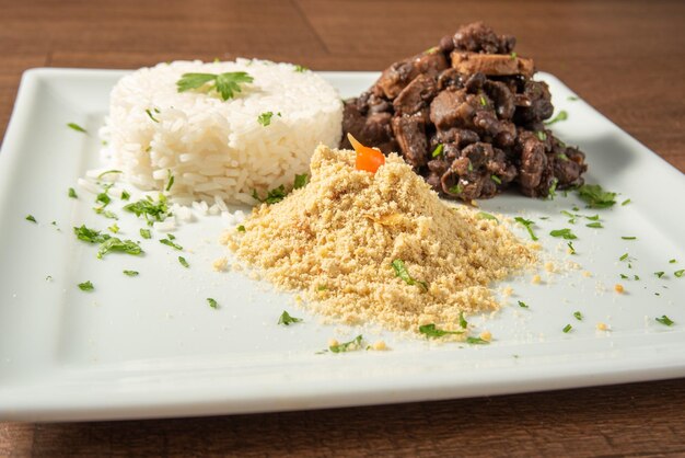 Comida vegana vegana feijoada arroz y farofa en un plato blanco sobre enfoque selectivo de madera