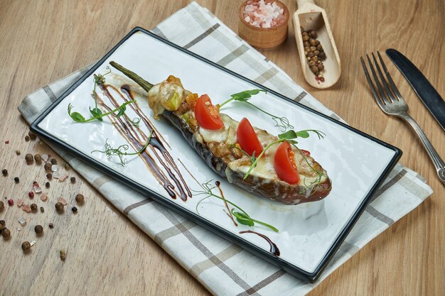 Comida vegetariana apetitosa - berinjela recheada assada com molho pesto e azeite de oliva em um prato de cerâmico em uma mesa de madeira. Fechar comida