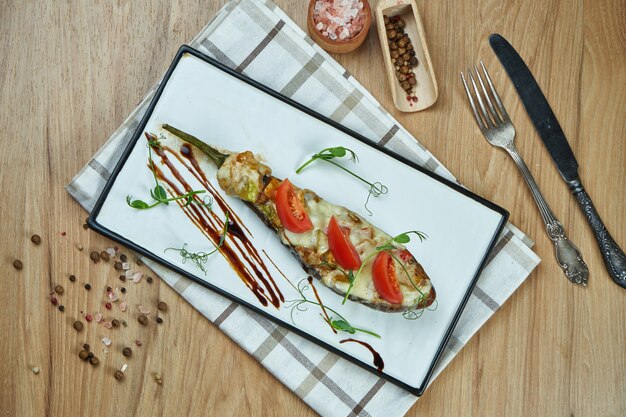 Comida vegetariana apetitosa - berinjela recheada assada com molho pesto e azeite de oliva em um prato de cerâmico em uma mesa de madeira. Fechar comida