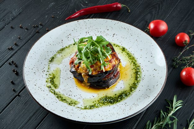 Comida vegetariana apetitosa - berinjela recheada assada com molho pesto e azeite de oliva em um prato de cerâmico em uma superfície de madeira. Fechar comida