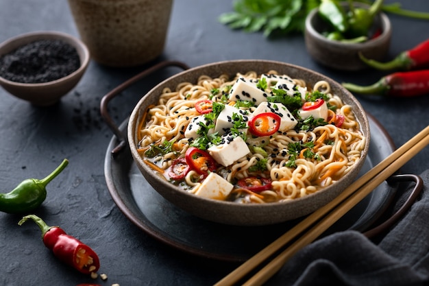 Comida vegetariana asiática, ramen con tofu y verduras en superficie oscura, enfoque selectivo