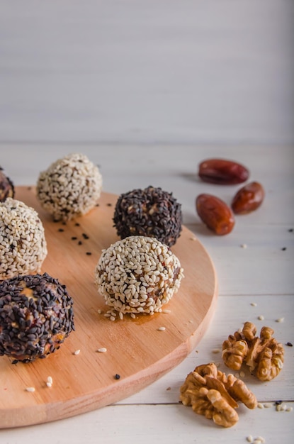 Comida vegetariana, bolas de energia caseiras de nozes, tâmaras, ameixas, cranberries e mel com gergelim branco e preto sobre fundo branco. Copie o espaço