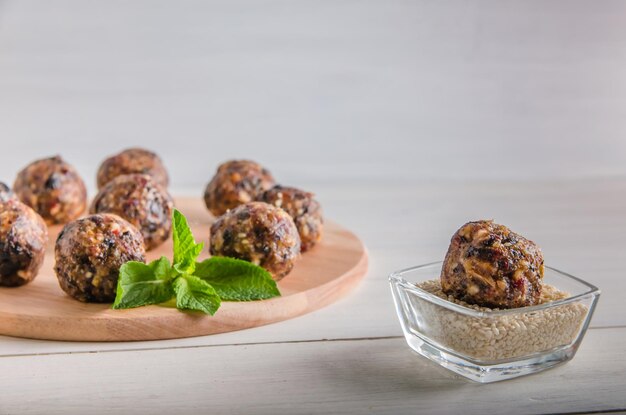 Comida vegetariana, bolas de energía caseras de nueces, dátiles, ciruelas pasas, arándanos y miel con sésamo sobre fondo blanco.