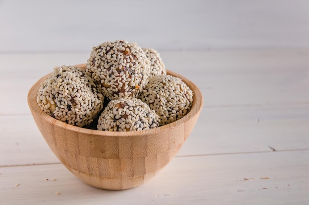 Comida vegetariana, bolas de energía caseras de nueces, dátiles, ciruelas pasas, arándanos y miel con sésamo sobre fondo blanco.