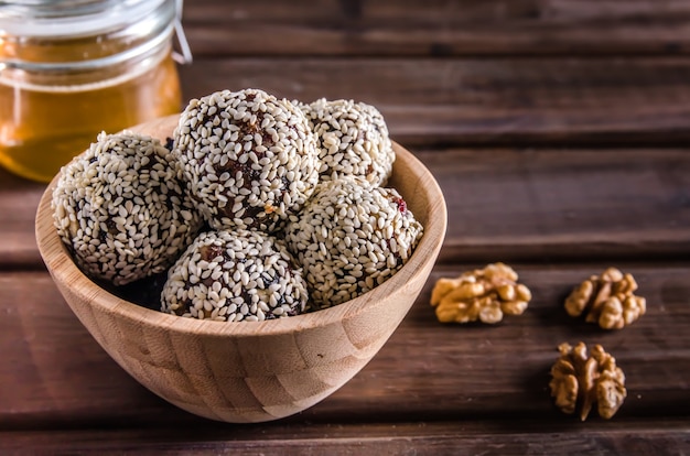 Comida vegetariana, bolas de energía caseras de nueces, dátiles, ciruelas pasas, arándanos y miel con sésamo sobre fondo de madera marrón