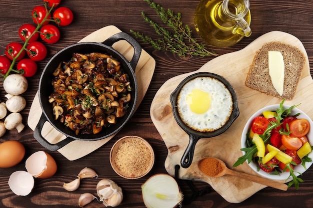 Comida vegetariana. Cogumelos fritos e ovo na panela de ferro fundido. Ingredientes para café da manhã rústico na mesa de madeira.