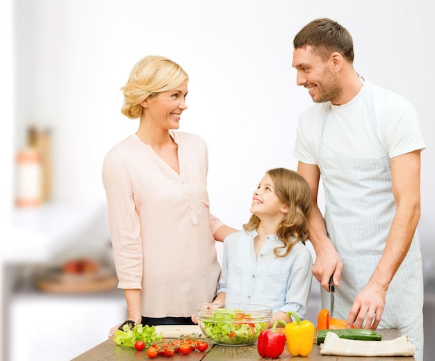 comida vegetariana, culinaria, felicidad y concepto de personas - familia feliz cocinando ensalada de verduras para la cena y hablando sobre el fondo de la cocina casera