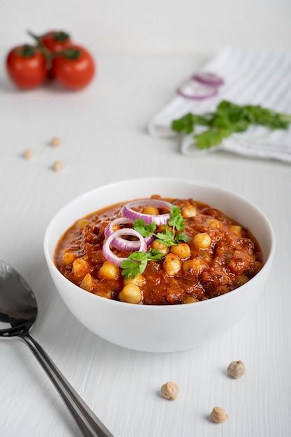 Comida vegetariana indiana Chole masala feita de grão de bico e tomate em uma tigela com uma colher na mesa de madeira