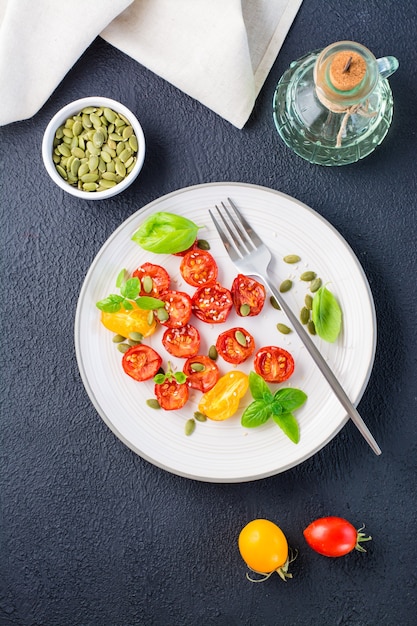 Comida vegetariana lista para consumir. Tomates secos con albahaca, semillas de sésamo y calabaza en un plato sobre un fondo negro. Vista superior y vertical