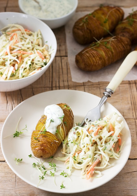 Comida vegetariana, patatas hasselback con salsa y ensalada de col sobre un fondo de madera. Estilo rústico