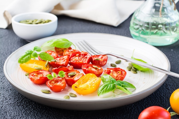 Comida vegetariana pronta para comer. Tomates secos com manjericão, sementes de gergelim e abóbora em um prato sobre um fundo preto