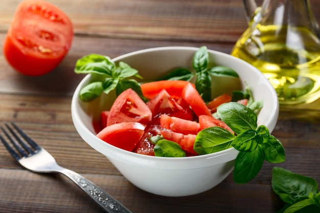 Comida vegetariana. Los tomates rojos frescos se cortan en rodajas en un plato de cerámica blanca con hierba de albahaca y aceite de oliva sobre una mesa de madera.