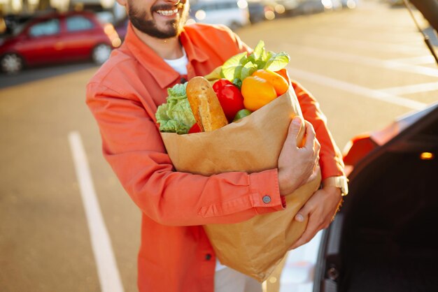 Foto comida vegetariana vegana saudável em um saco de papel nas mãos masculinas homem com sacola de compras perto do carro