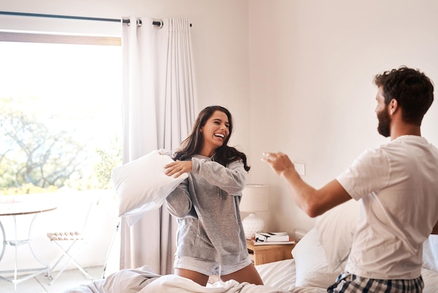 Comience cada mañana con tonterías Foto de una feliz pareja joven teniendo una pelea de almohadas en la cama