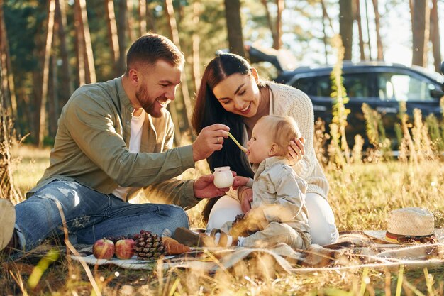 Comiendo algo de comida una familia feliz de padre madre y hija pequeña está en el bosque