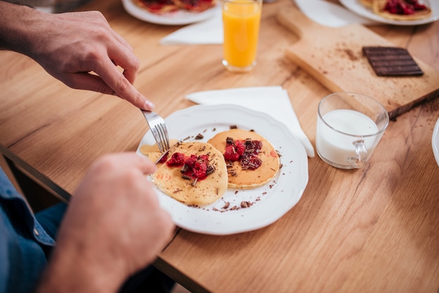 Comiendo las crepes deliciosas con la bifurcación y el cuchillo en la tabla de madera, primer.