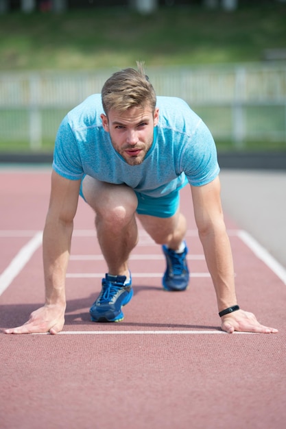 Comienzo de la carrera deportiva Hombre corredor en la posición de inicio fondo del estadio Deportista correr al aire libre en la pista de atletismo Posición de inicio del corredor superficie de carrera Deportista en la cara concentrada listo para ir