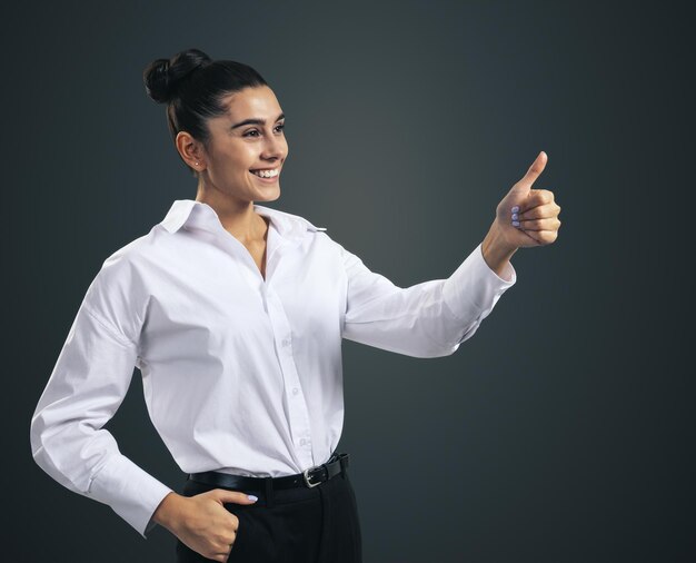 Como concepto con feliz joven empresaria en camisa blanca sosteniendo los pulgares hacia arriba sobre fondo de pared negra de cerca aislado