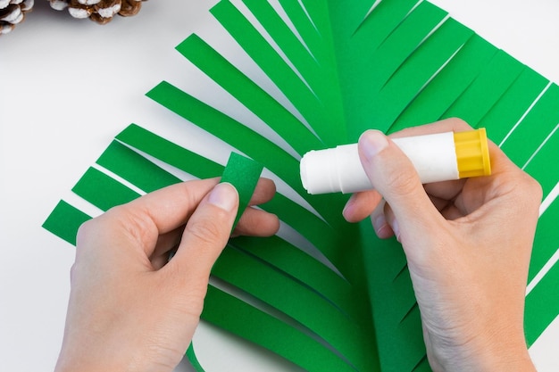 Como fazer uma árvore de Natal criativa com papel colorido e cola com as próprias mãos. Conceito de DIY. Instruções passo a passo.