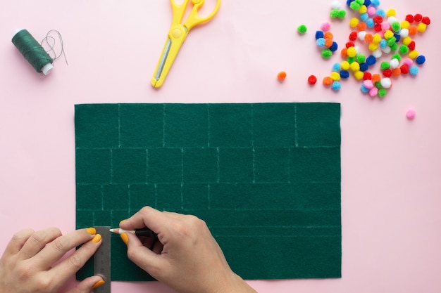 Como fazer uma pequena árvore de natal de feltro em casa. Instruções passo a passo. Mãos facilitando o acompanhamento do projeto DIY.