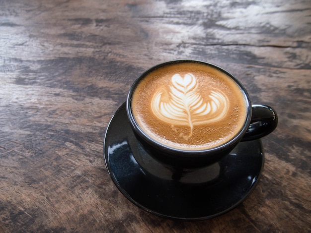 Cómo hacer café latte art en una taza negra, poner en una mesa de madera vieja. En una cafeteria