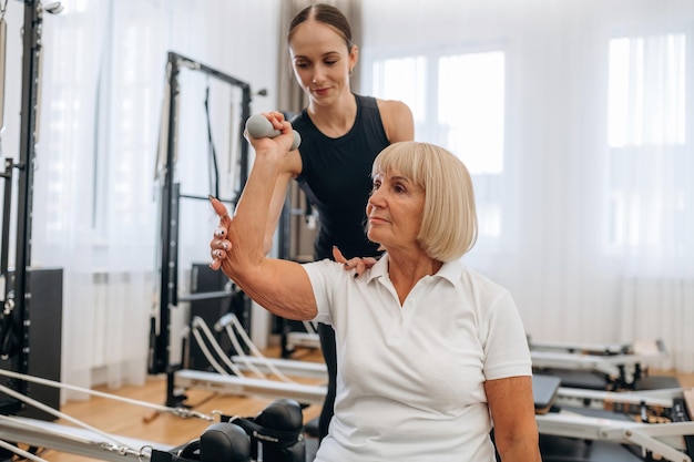 Cómo levantar la manivela La entrenadora está ayudando a la anciana a hacer ejercicio