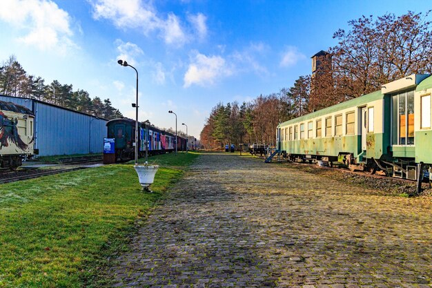 Foto como limburg bélgica diciembre 17 2023 camino adoquinado en la antigua estación de tren vías en desuso con camiones de carga y pasajeros árboles desnudos contra el cielo azul en el fondo día soleado