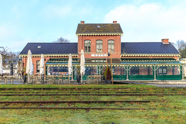 Foto como limburg bélgica diciembre 17 2023 fachada del restaurante asch en el edificio de la antigua terraza de la estación de tren con sillas y mesas vías en desuso frente al día nublado