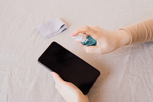 Como limpar, higienizar seu telefone em casa. mãos de mulher, limpeza smartphone por spray desinfetante.