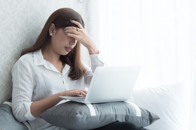 Como una mujer tiene fiebre, le duele la cabeza cuando usa su computadora portátil en el dormitorio.