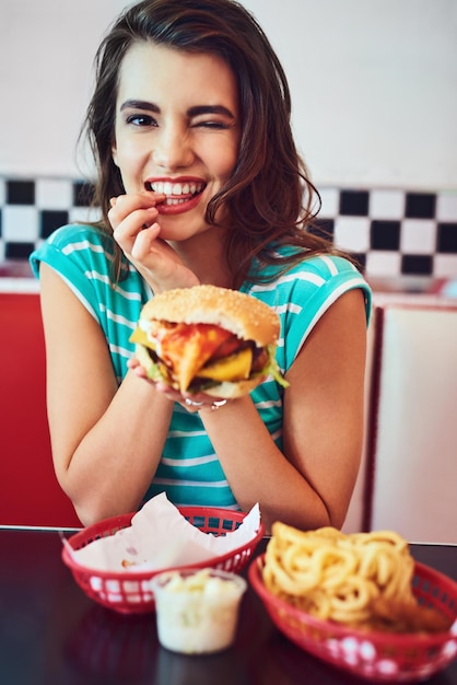 Como muy bien Retrato recortado de una joven atractiva disfrutando de una hamburguesa en un restaurante retro