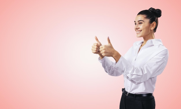 Como o conceito com uma garota feliz na camisa branca segurando os polegares no fundo da parede rosa claro com lugar vazio para você texto simulado