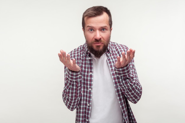 Como pudiste. Retrato de un hombre barbudo disgustado con un pantalones a cuadros casual levantando las manos mirando confundido y descontento con la cámara, esperando una explicación. Foto de estudio interior aislado sobre fondo blanco.